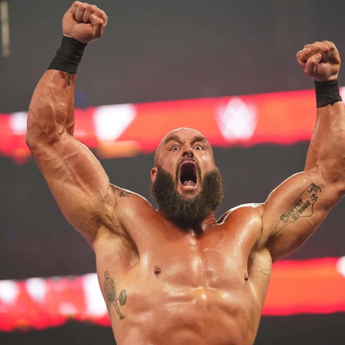 WWE 桌布 壁紙 — 一位肌肉發達、光頭、留鬍子的摔角手在明亮的燈光下於摔角台上高舉雙拳，勝利地吶喊。