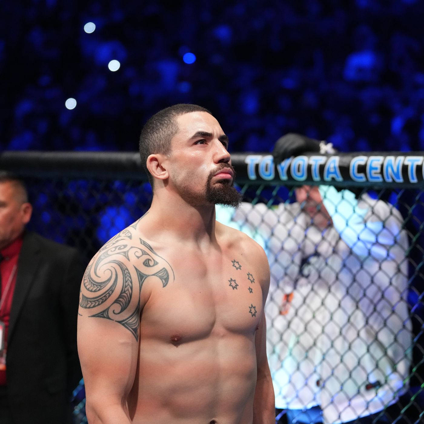 UFC 桌布 壁紙 — 一位肌肉發達、帶有部落紋身的戰士站在燈火通明的八角籠內，在人群面前專注地向上凝視。
