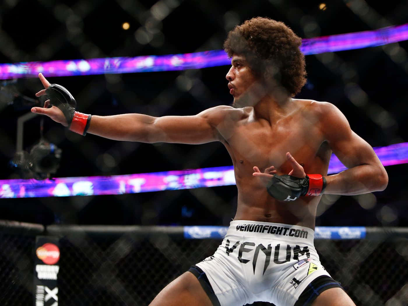 MMA 桌布 壁紙 — 一位肌肉發達、捲髮的拳手在燈光明亮的八角籠中出擊，背景有紫色燈光和模糊的籠子。