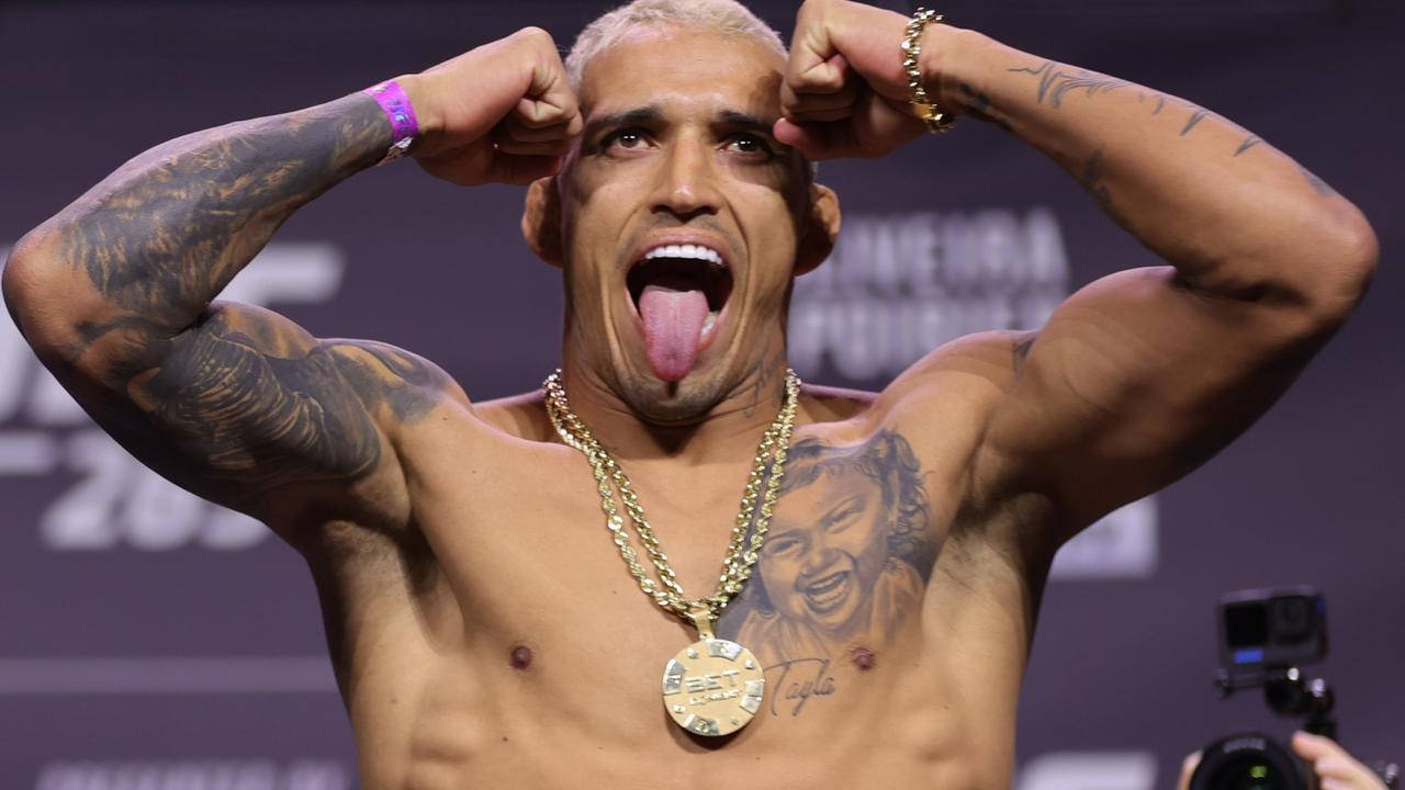 MMA 桌布 壁紙 — 一位肌肉發達、有刺青、金髮、戴金鏈的拳手在稱重台上彎曲手臂並伸出舌頭。