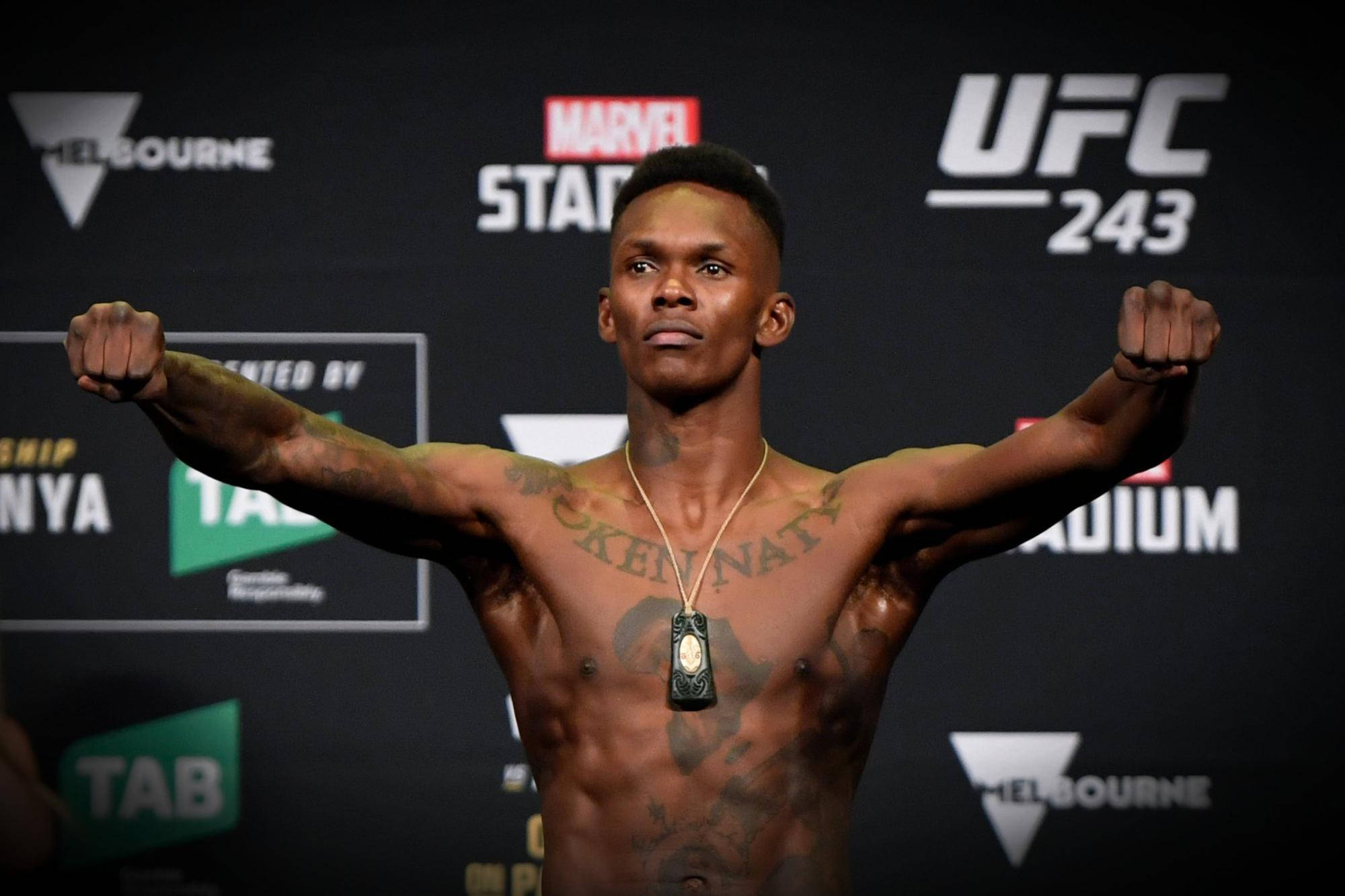 Adesanya 桌布 壁紙 — 一位肌肉發達、有刺青的拳手在 UFC 稱重活動中自信地舉起雙臂。
