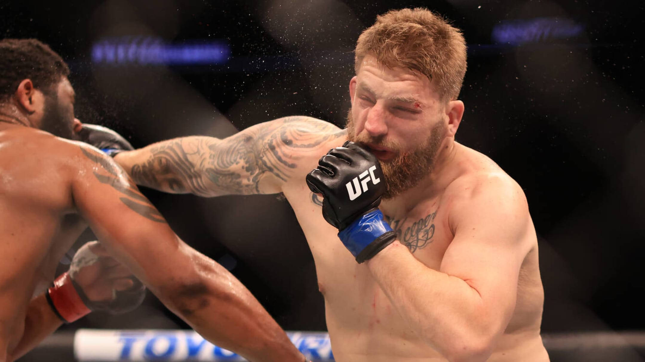 Punch 桌布 壁紙 — 一位肌肉發達、有刺青的拳手在UFC八角籠中打出強力一拳，汗水在場館燈光下飛濺。