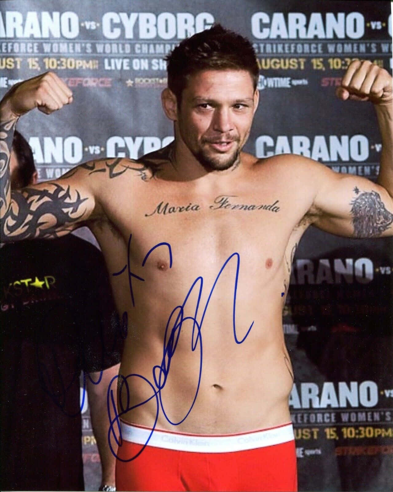 MMA 桌布 壁紙 — 一位肌肉發達、有刺青的拳手在稱重活動中赤裸上身展示肌肉，身後有宣傳橫幅。