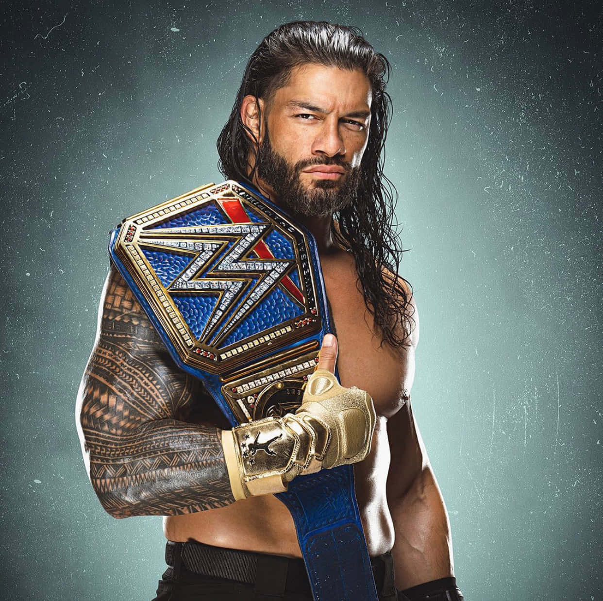 WWE 桌布 壁紙 — 一位肌肉發達、留著深色長髮並有刺青的摔角手，在紋理灰色背景前手持藍金色冠軍腰帶。