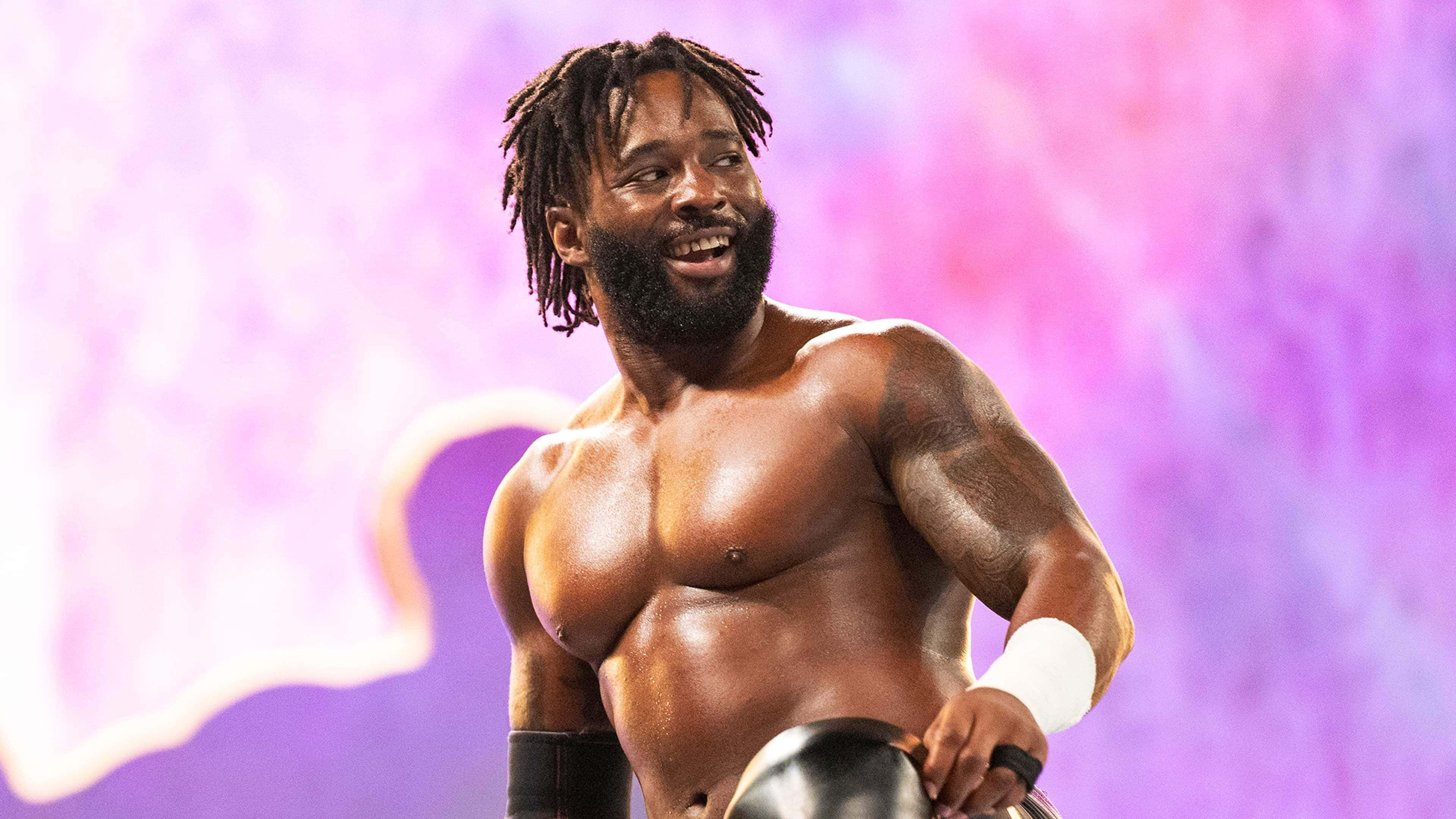 WWE 桌布 壁紙 — 一位肌肉發達、留著辮子和鬍鬚的摔角手，在充滿活力的紫色和粉紅色背景前自信地咧嘴笑著，同時手持冠軍腰帶。