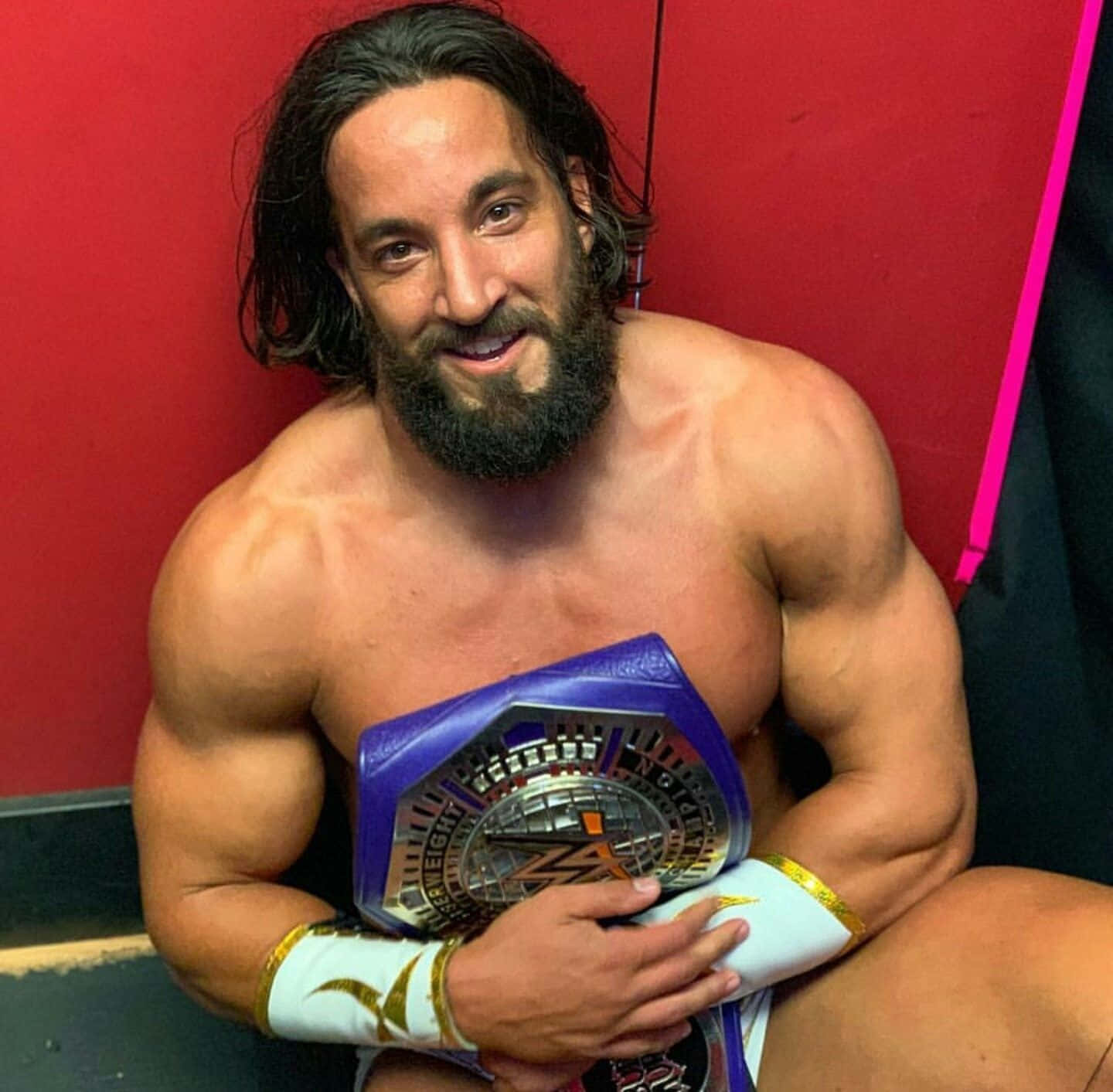 WWE 桌布 壁紙 — 一位肌肉發達、留著長黑鬍子的摔角手，在紅色牆壁前自豪地微笑，手持一條紫色和銀色的冠軍腰帶。