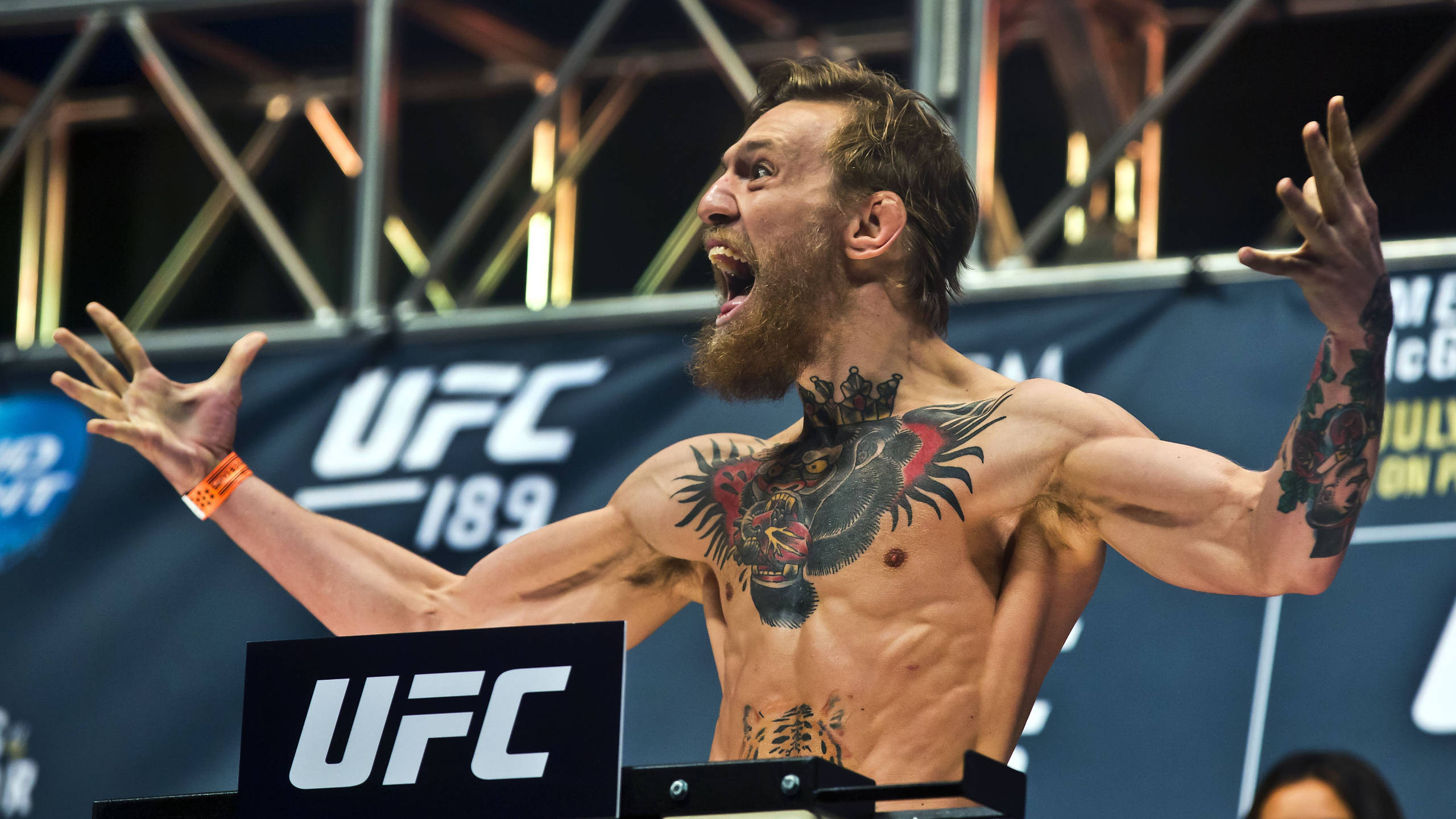 Mcgregor 桌布 壁紙 — 一位肌肉發達、留鬍子、有紋身的拳手在明亮的場館燈光下，在 UFC 賽事中高舉雙臂，發出勝利的怒吼。