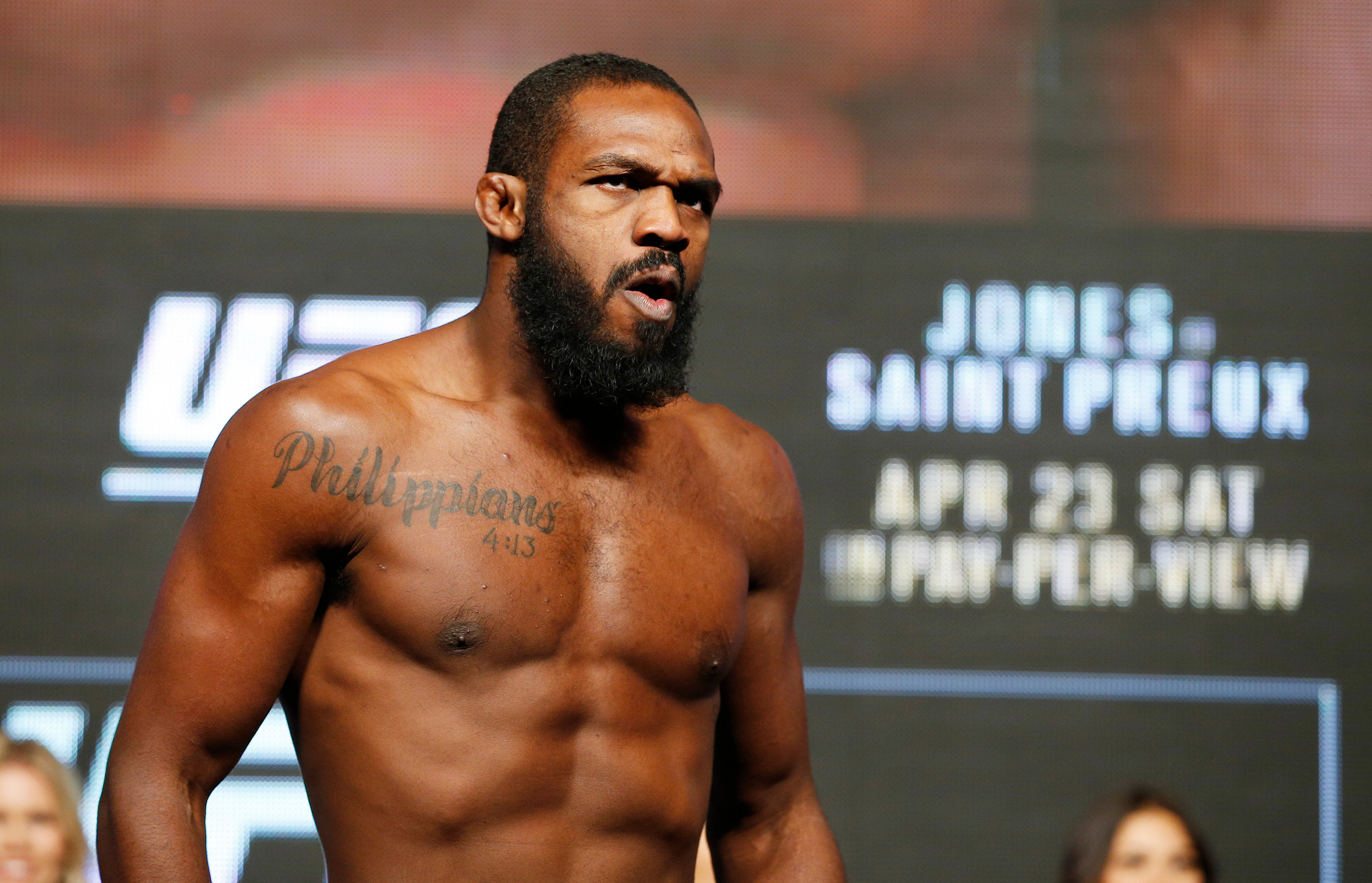 UFC 桌布 壁紙 — 一位肌肉發達、留鬍子的戰士，身上有「腓立比書 4:13」的刺青，在 UFC 稱重背景前凝視著。