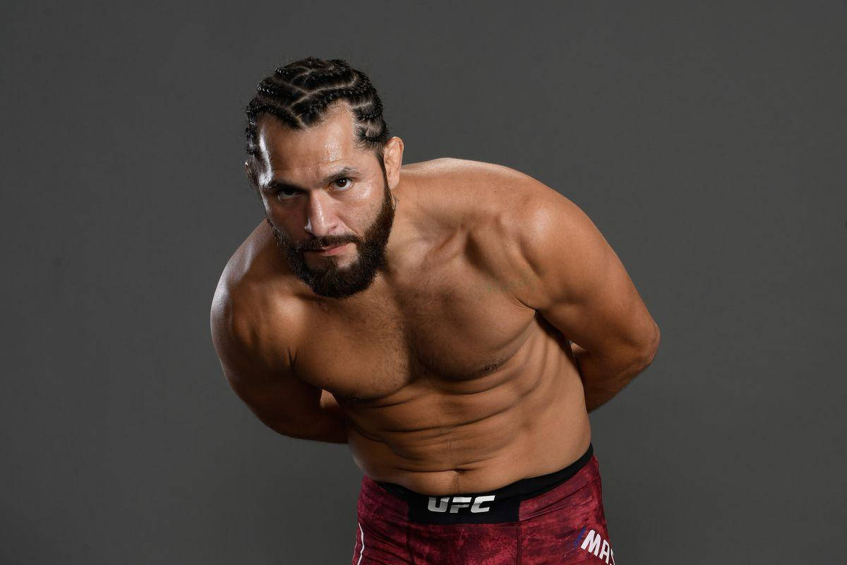 UFC 桌布 壁紙 — 一位肌肉發達、留鬍子的戰士穿著紅色UFC短褲，在灰色工作室背景前專注地向前傾身。