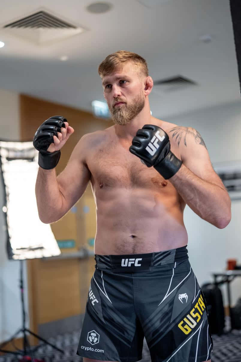 UFC 桌布 壁紙 — 一位肌肉發達、留鬍子的戰士身穿UFC裝備，在健身房舉起拳頭準備戰鬥。