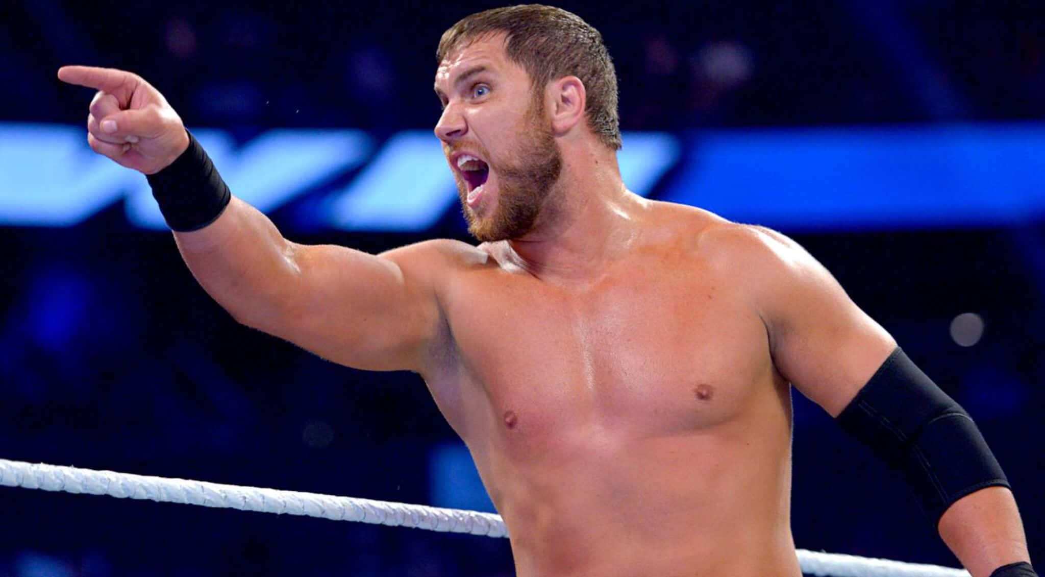 WWE 桌布 壁紙 — 一位肌肉發達、留鬍子的摔角手在明亮的場館燈光下，在擂台上大喊並勝利地指著。