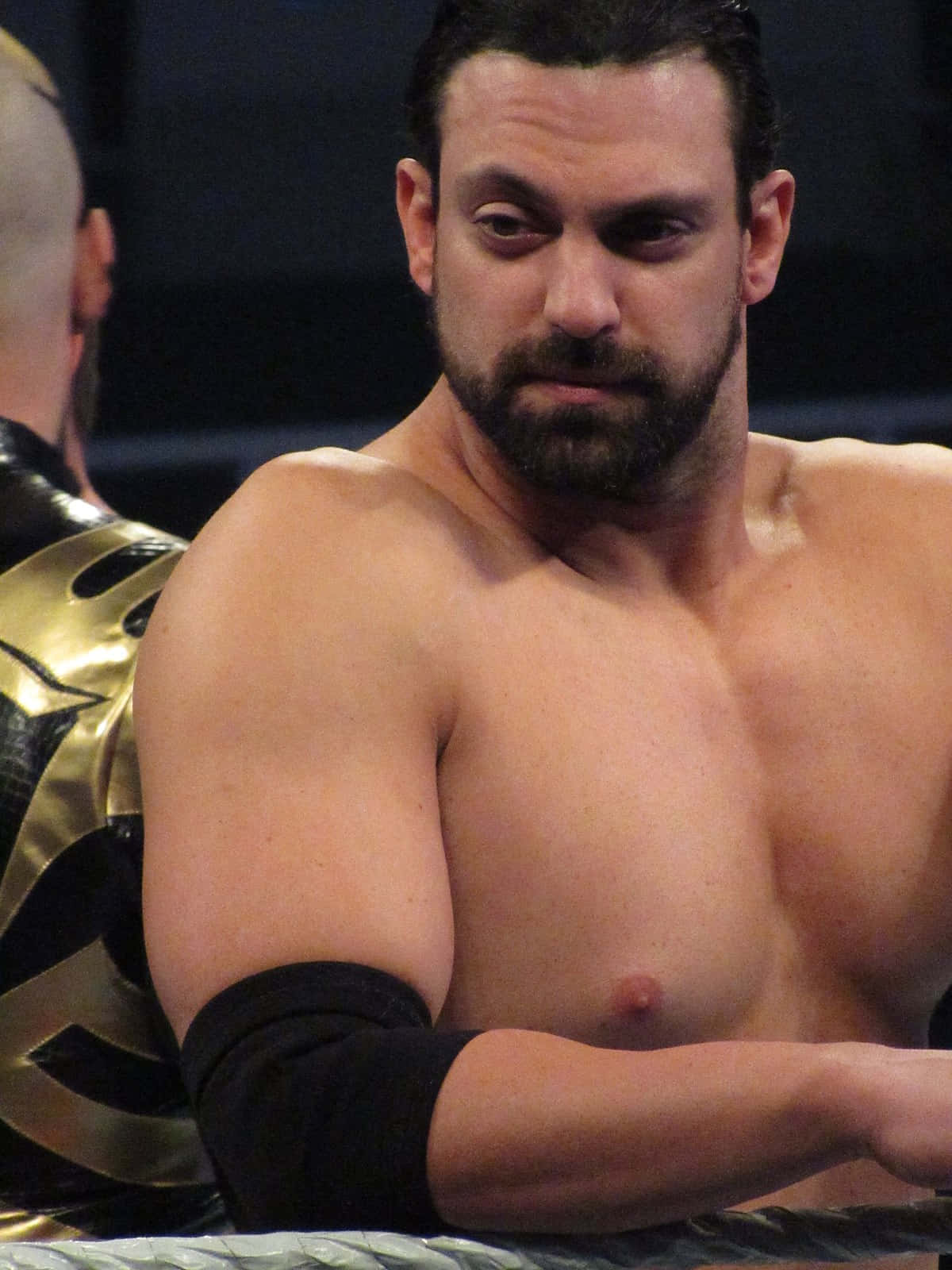 WWE 桌布 壁紙 — 一位肌肉發達、留鬍子的摔角手在昏暗的競技場中靠在擂台繩索上，眼神銳利。