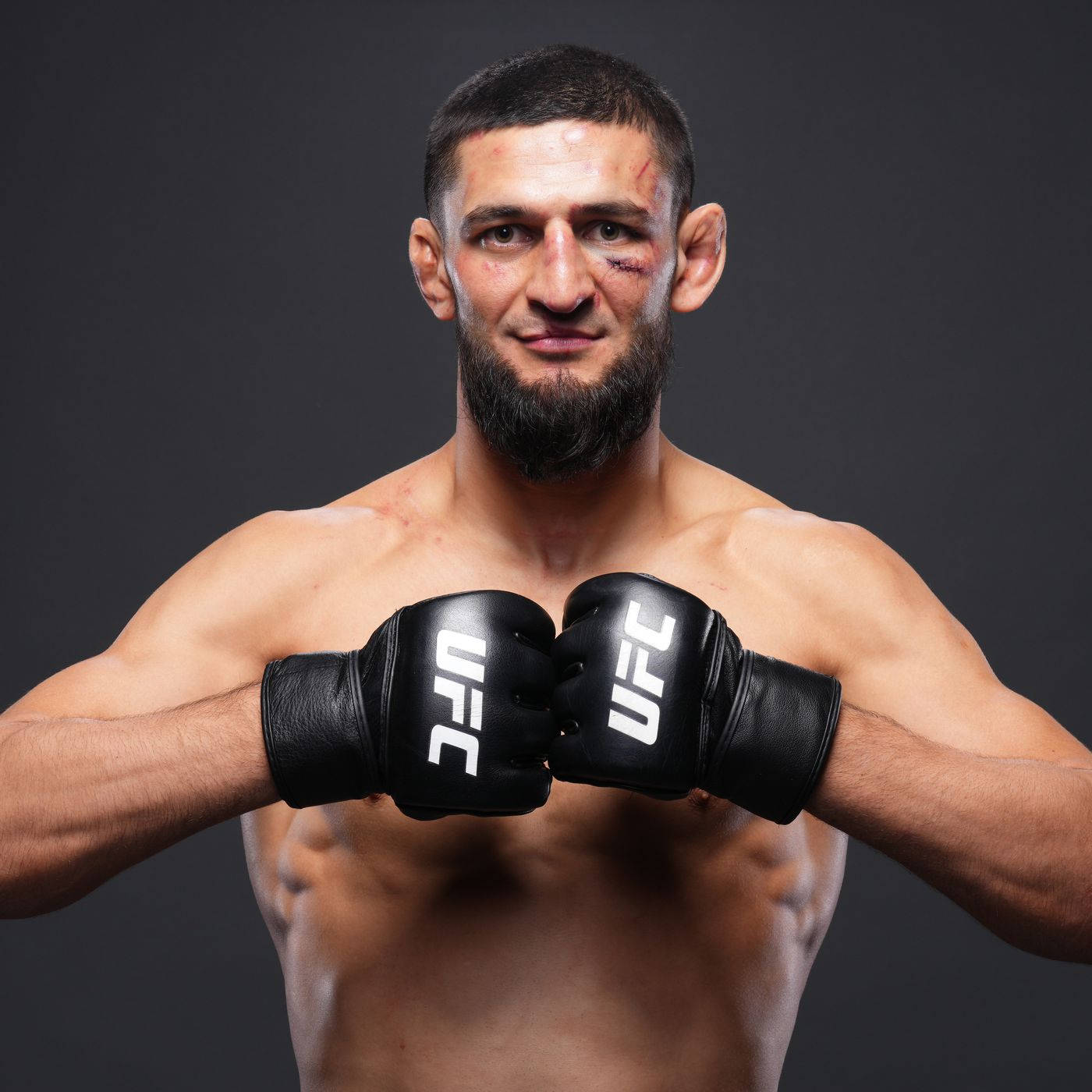 MMA 桌布 壁紙 — 一位肌肉發達、留鬍鬚且臉部有瘀傷的UFC拳擊手，在黑色工作室背景下自信地戴著黑色手套擺姿勢。