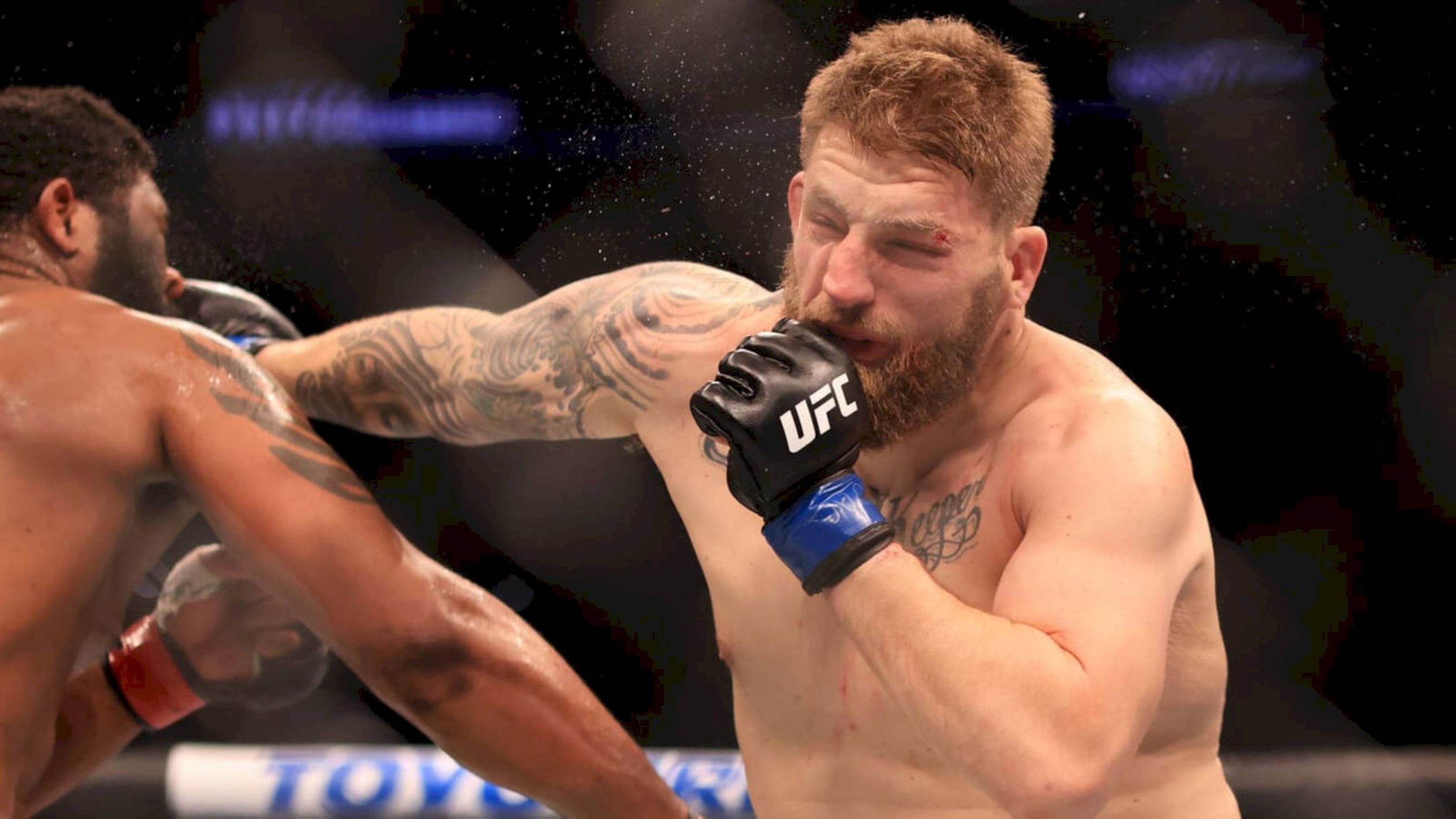 Punch 桌布 壁紙 — 一位肌肉發達、紋身的拳手在UFC比賽中打出強力一拳，汗水在場館燈光中飛濺。