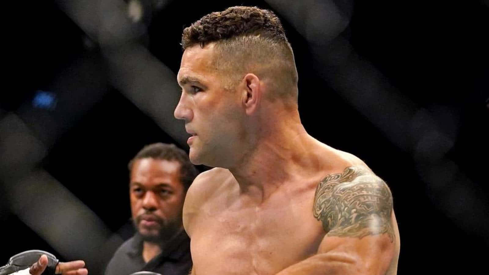 MMA 桌布 壁紙 — 一位肌肉發達、肩膀有刺青的拳手在昏暗的八角籠內的新聞發布會上專注地凝視。