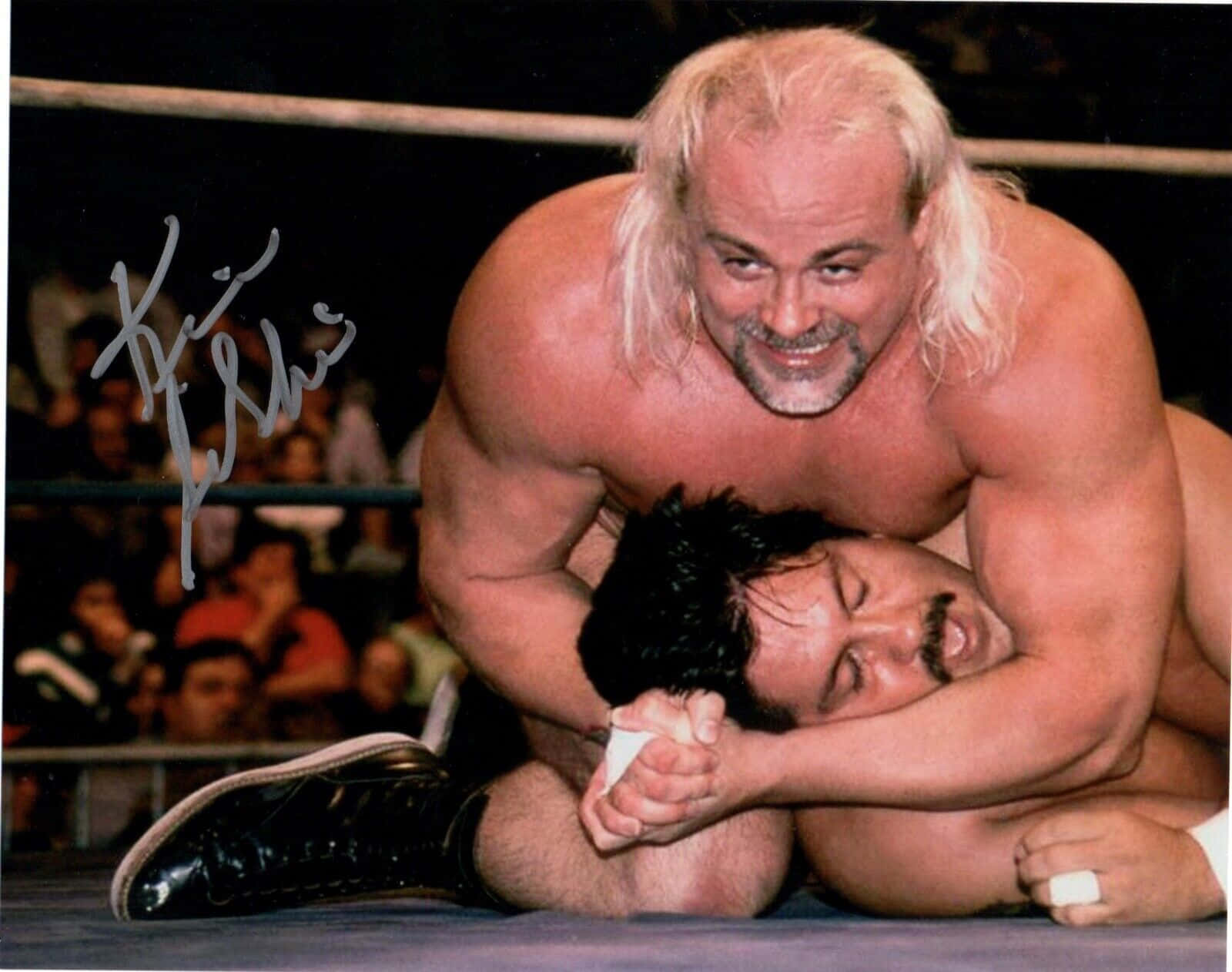 WWE 桌布 壁紙 — 一位肌肉發達、長白髮的摔角手在明亮燈光下咧嘴笑著，將對手壓制在摔角台上。