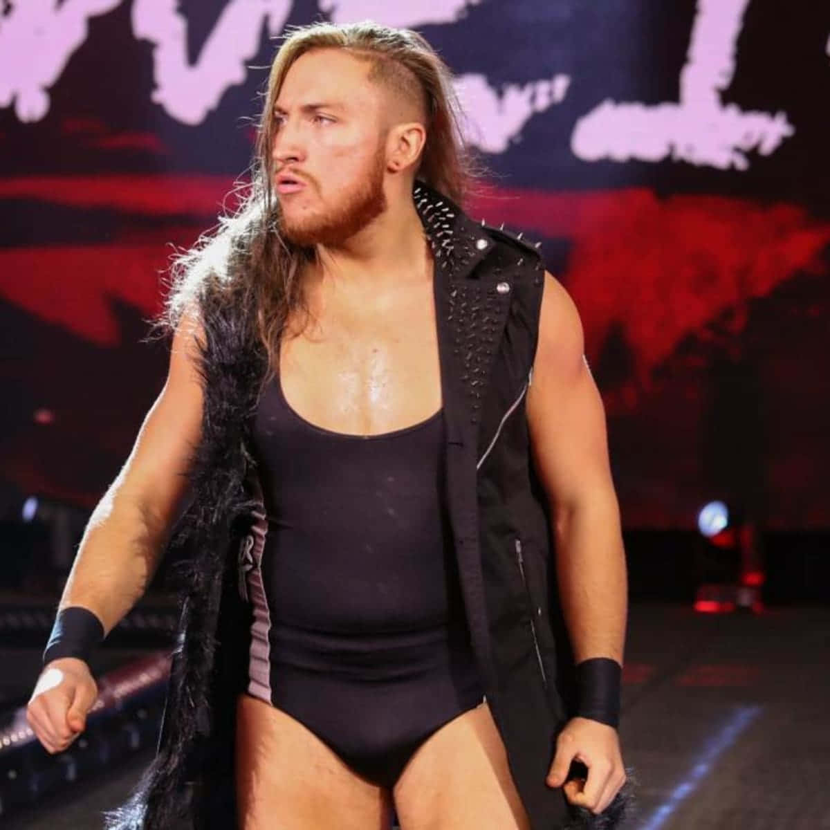Wrestling 桌布 壁紙 — 一位肌肉發達、長髮鬍鬚的摔角手，穿著黑色鉚釘背心和緊身衣，在場館燈光下自信地走著。