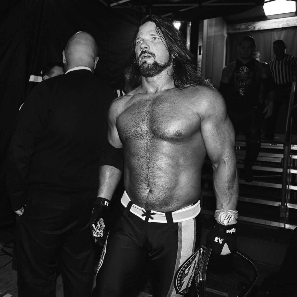 WWE 桌布 壁紙 — 一位肌肉發達、長髮鬍鬚的摔角手，赤裸上身站在後台，在戲劇性的黑白燈光下手持冠軍腰帶。