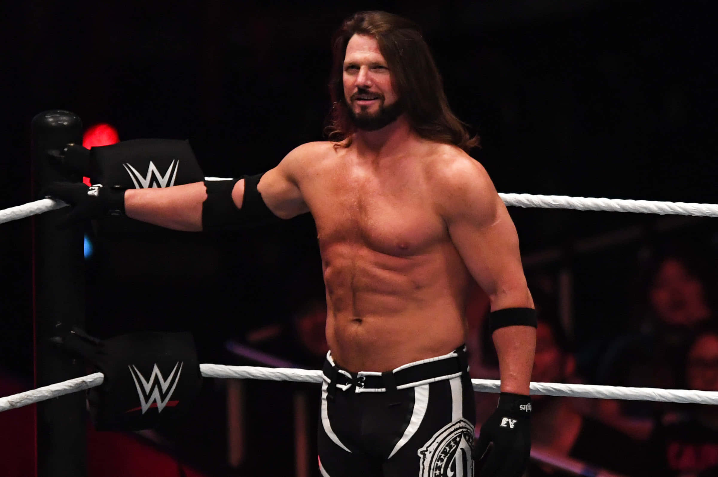 WWE 桌布 壁紙 — 一位肌肉發達、長髮鬍鬚的摔角手自信地站在摔角場上，穿著黑白短褲和手套。