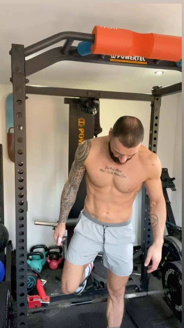 Fitness 桌布 壁紙 — 一位肌肉發達且有刺青的男士在家中的健身房內，周圍環繞著壺鈴和重量訓練器材，進行單腿深蹲。