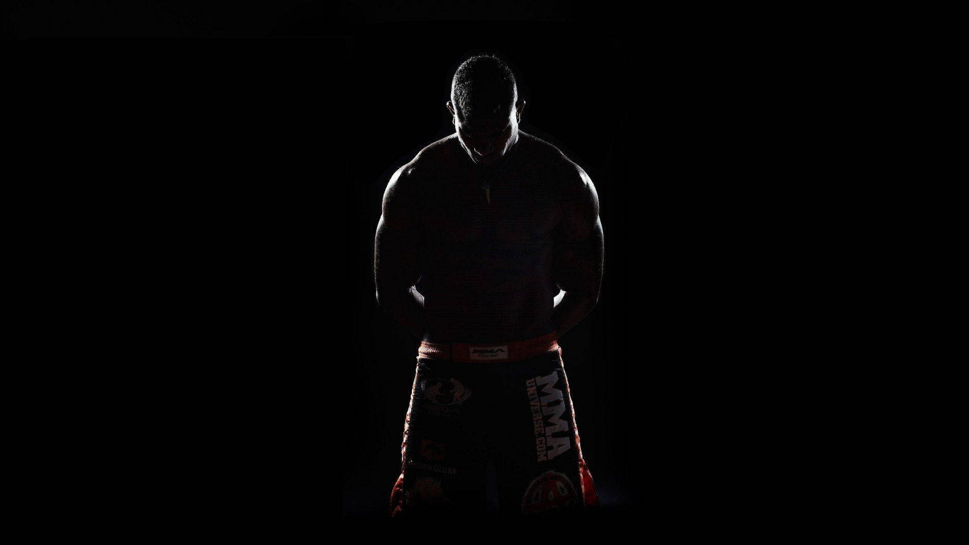 Boxing 桌布 壁紙 — 一位肌肉發達的MMA拳手以剪影姿態站在黑色背景前，短褲上有微弱的紅色飾邊。