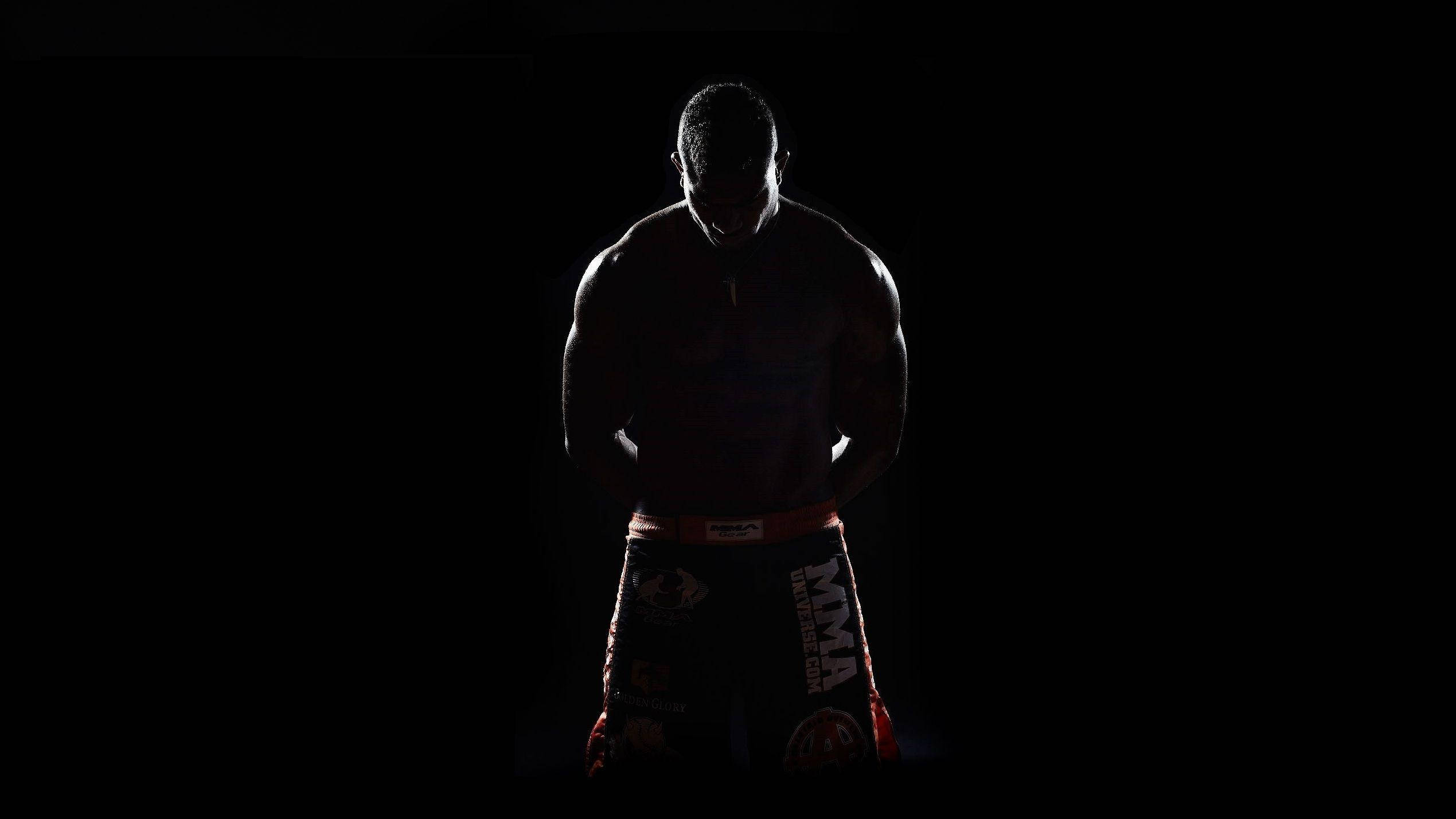 MMA 桌布 壁紙 — 一位肌肉發達的MMA拳手以剪影姿態站在黑色背景前，短褲帶有微弱的紅色飾邊。