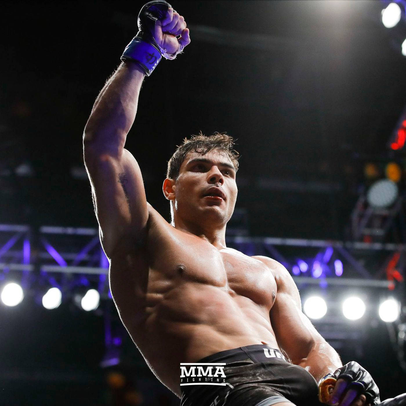 UFC 桌布 壁紙 — 一位肌肉發達的MMA拳手在明亮的場館燈光下，勝利後高舉戴著手套的拳頭。