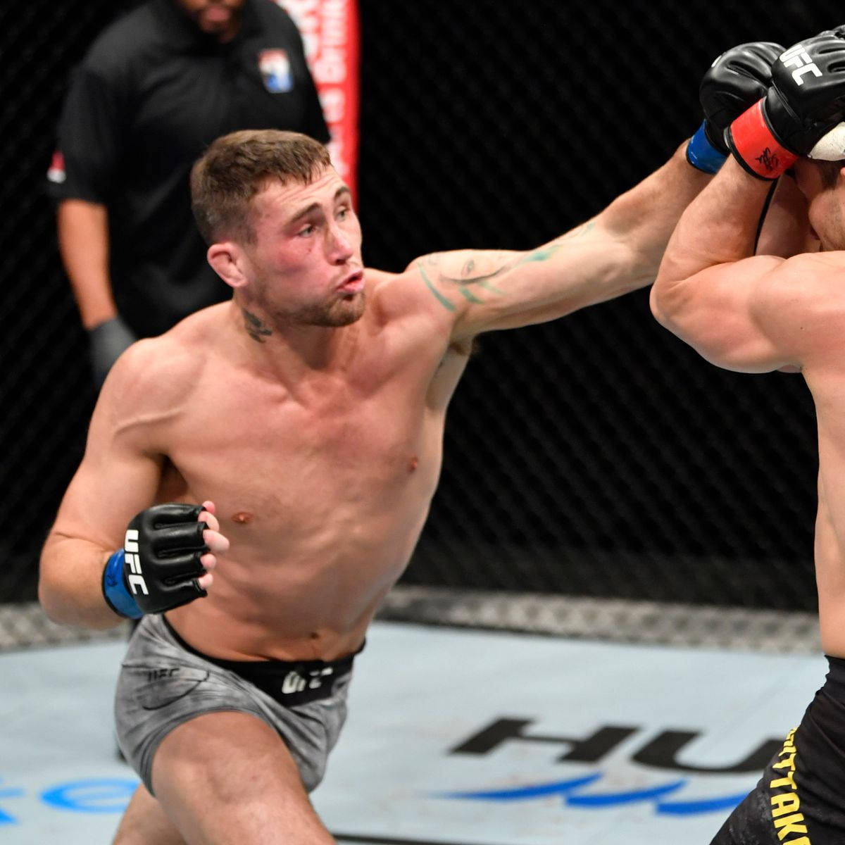 UFC 桌布 壁紙 — 一位肌肉發達的MMA拳手在明亮的場館燈光下，於UFC八角籠內向對手打出強力一拳。