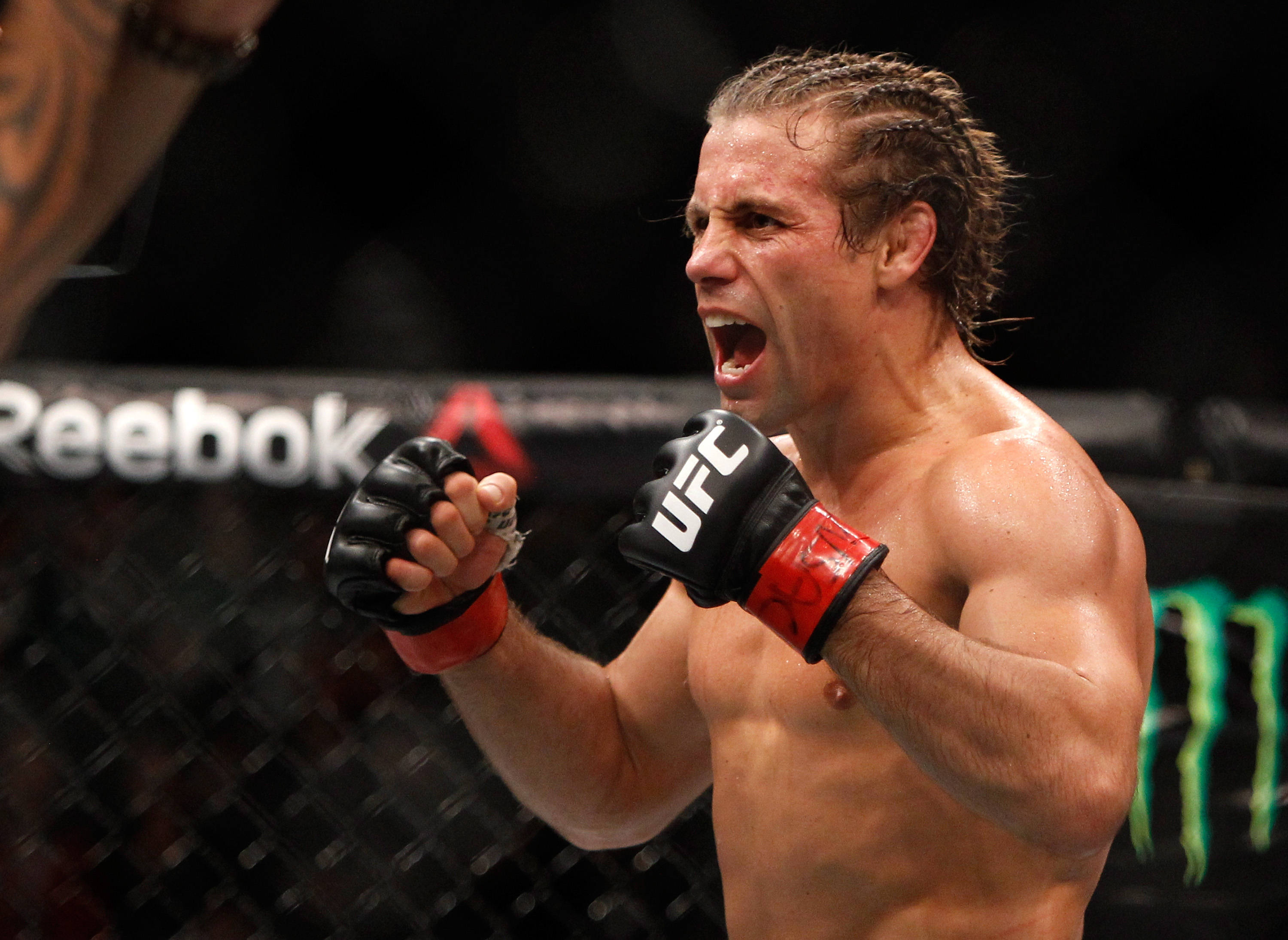 UFC 桌布 壁紙 — 一位肌肉發達的MMA拳手在籠內戴著UFC手套，汗水在皮膚上閃閃發光，發出勝利的咆哮。