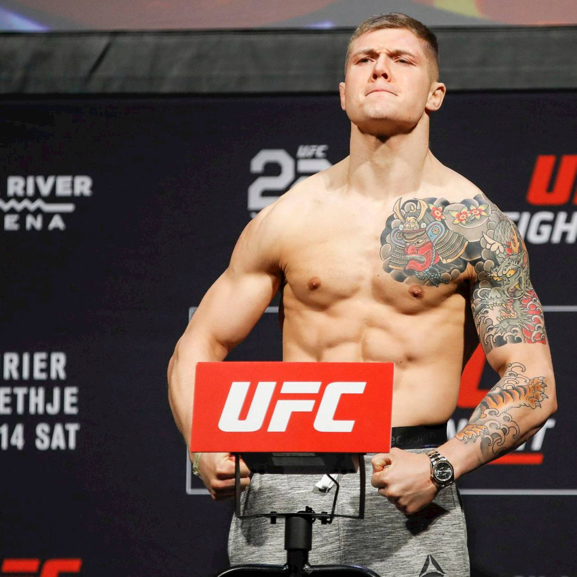 MMA 桌布 壁紙 — 一位肌肉發達的UFC拳手，帶有精緻的袖套紋身，在稱重活動中赤膊站在體重秤上。