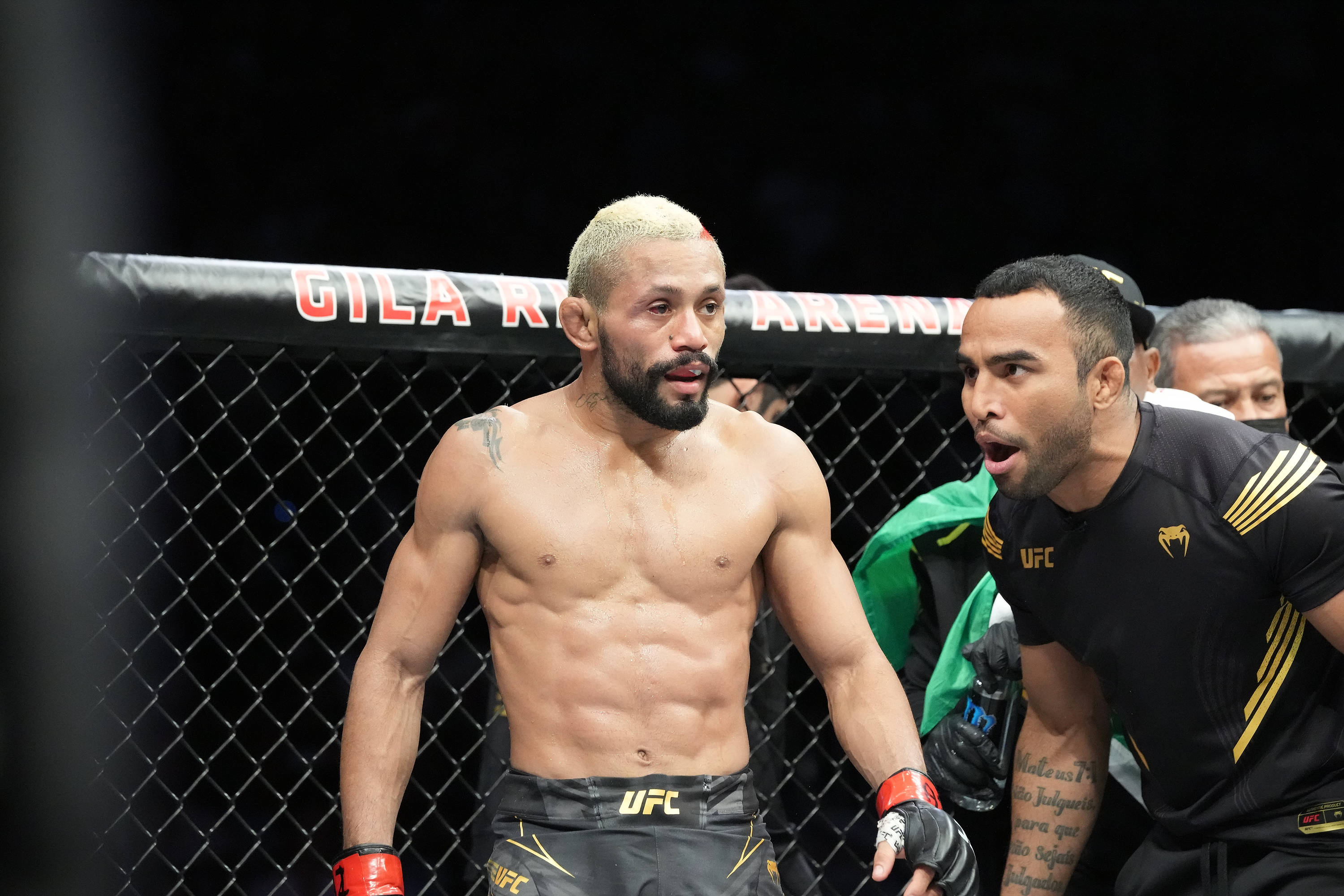 UFC 桌布 壁紙 — 一位肌肉發達的UFC拳手，漂染了頭髮和鬍鬚，站在八角籠內，教練在休息期間急切地靠過來。