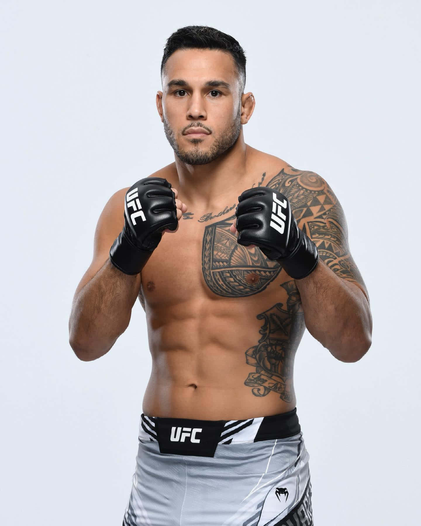 MMA 桌布 壁紙 — 一位肌肉發達的UFC拳手，身上有刺青，在純白色背景前擺出戰鬥姿勢，戴著黑色手套和灰色短褲。