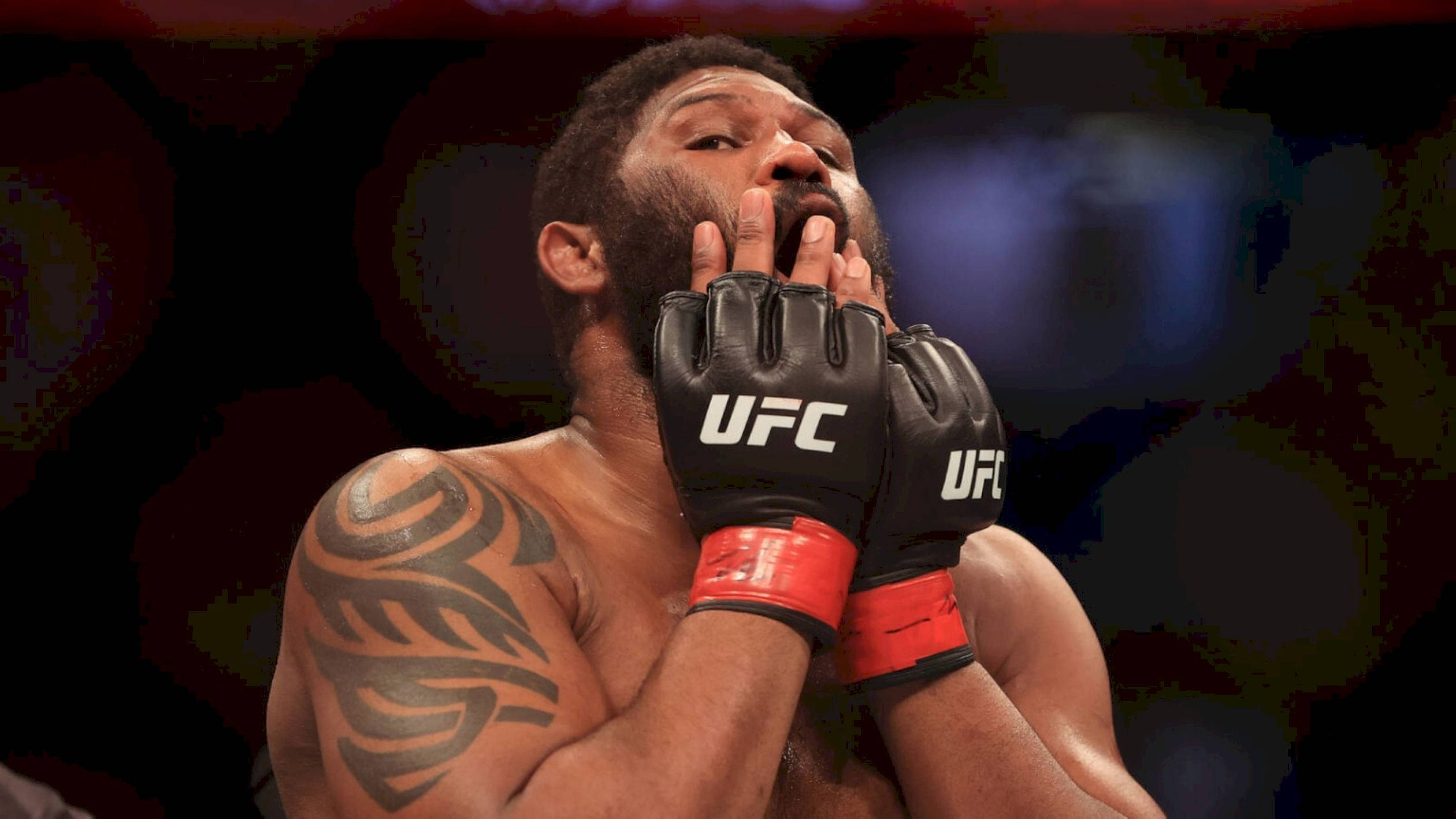 UFC 桌布 壁紙 — 一位肌肉發達的UFC拳手，身上有部落紋身，在八角籠內因疲憊或情緒而掩嘴。