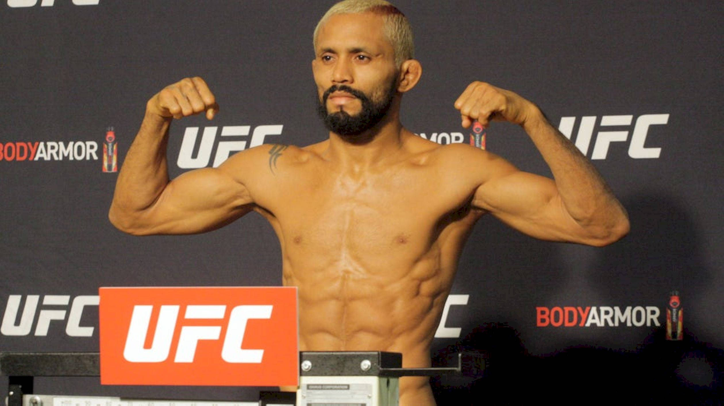 MMA 桌布 壁紙 — 一位肌肉發達的UFC拳手在品牌背景前於磅秤上彎曲手臂。