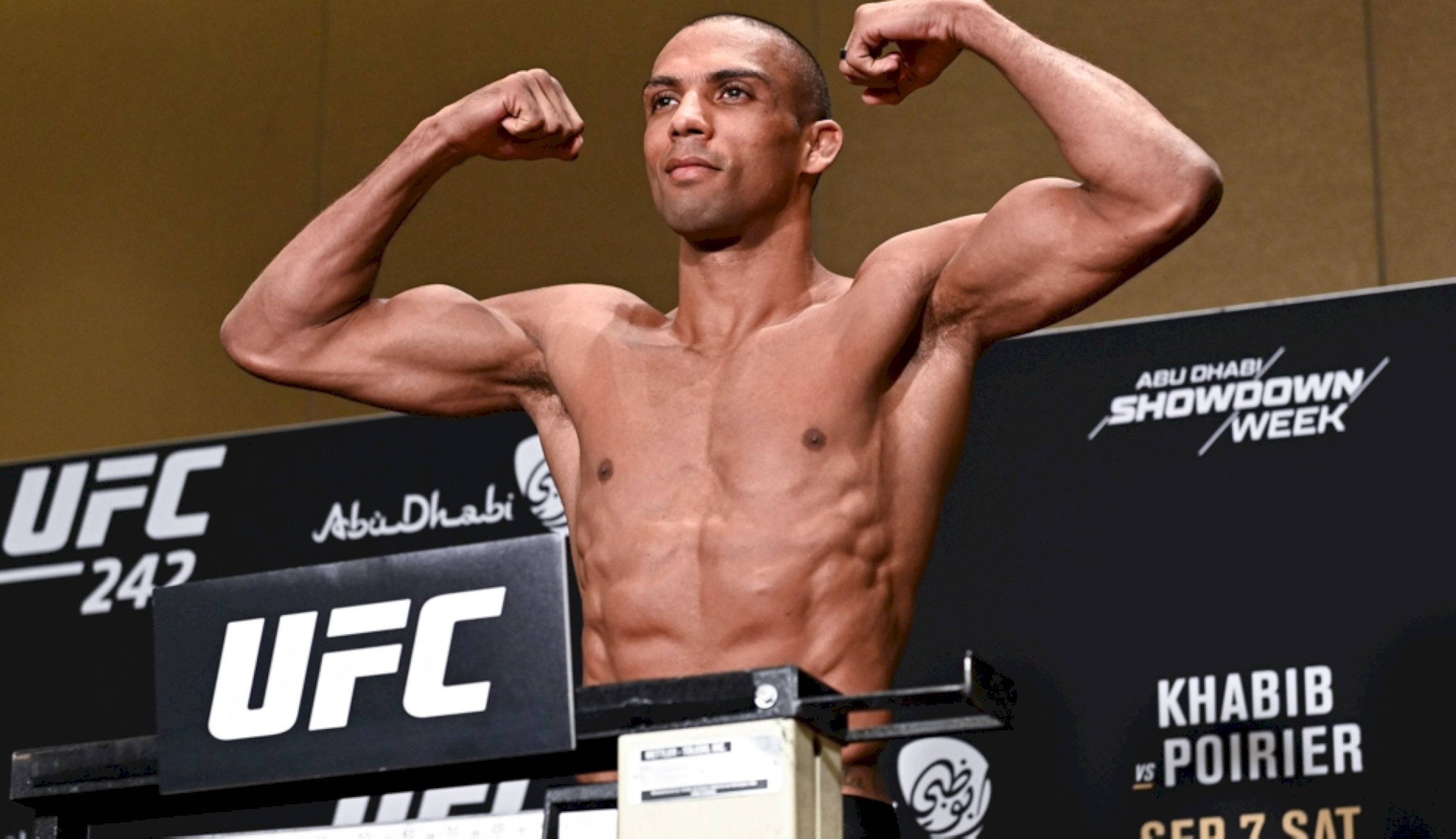 MMA 桌布 壁紙 — 一位肌肉發達的UFC拳手在帶有「Abu Dhabi Showdown Week」品牌的稱重活動中，在體重磅上屈曲手臂。