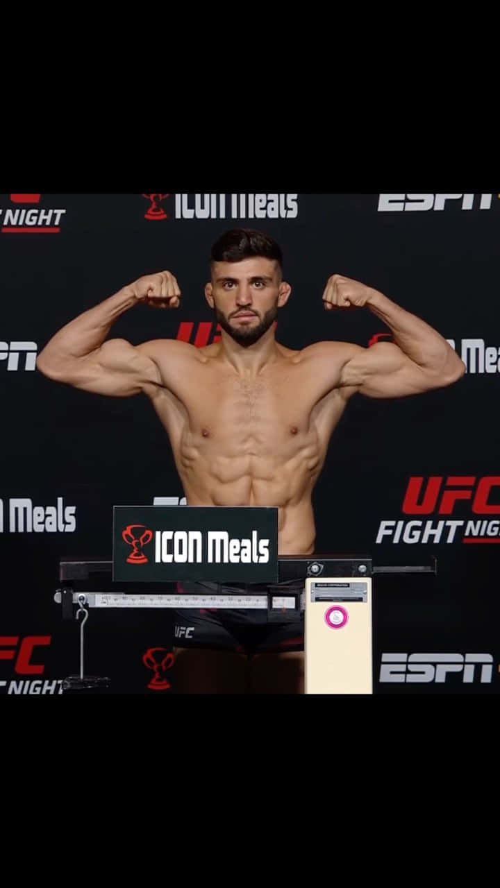 UFC 桌布 壁紙 — 一位肌肉發達的UFC拳手在帶有ESPN和ICON Meals品牌的稱重活動中，在磅秤上彎曲手臂。