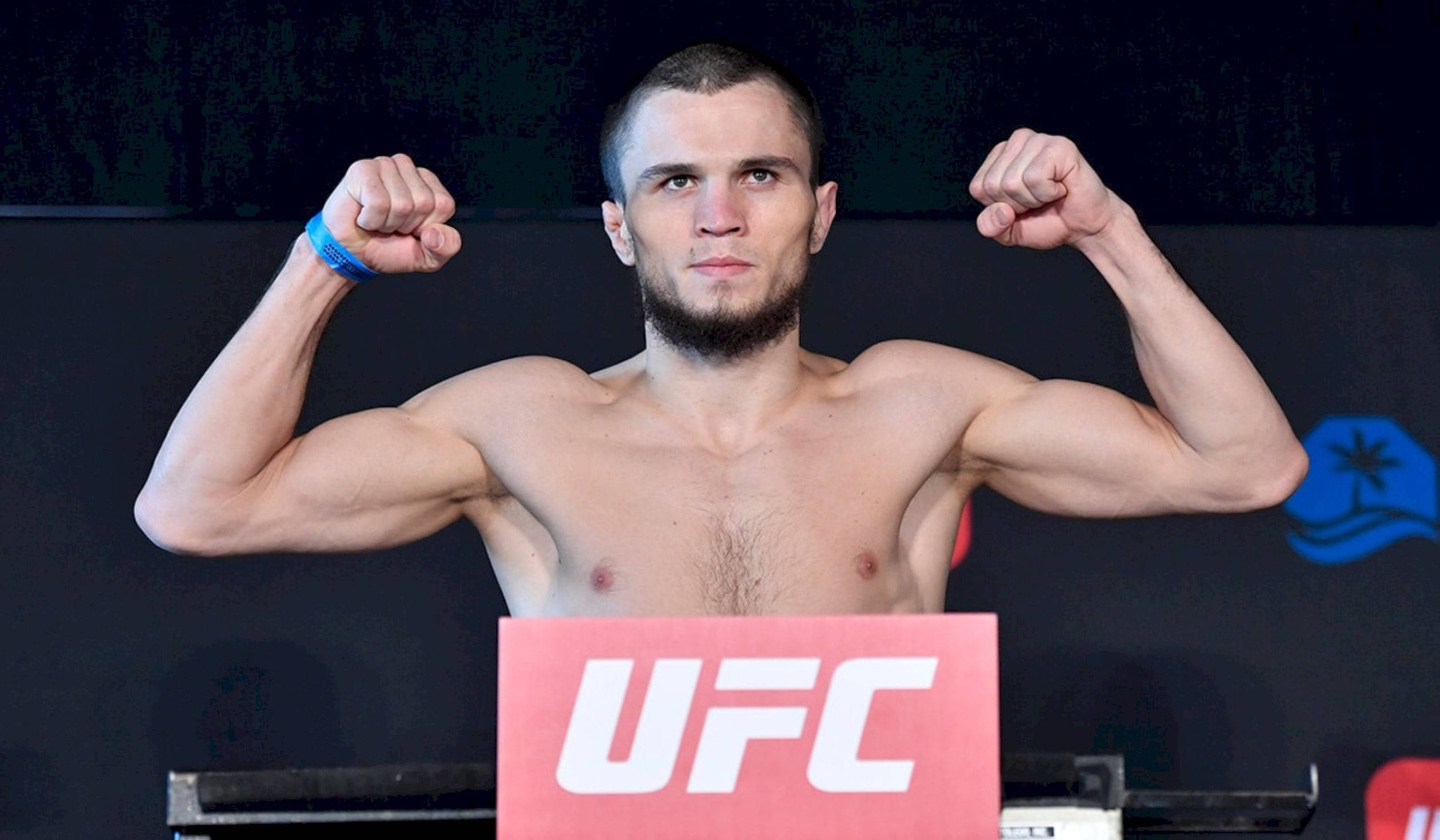 UFC 桌布 壁紙 — 一位肌肉發達的UFC拳手在明亮的攝影棚燈光下，於過磅活動中雙臂彎曲，神情專注。