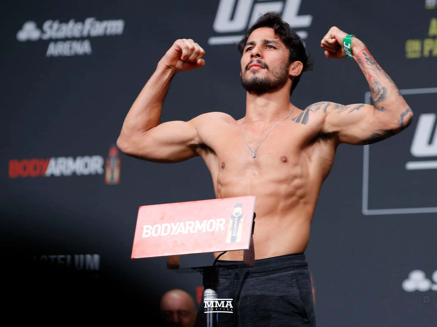 MMA 桌布 壁紙 — 一位肌肉發達的UFC拳手在秤重活動中，於體重磅上屈起手臂，背後有贊助商標誌。