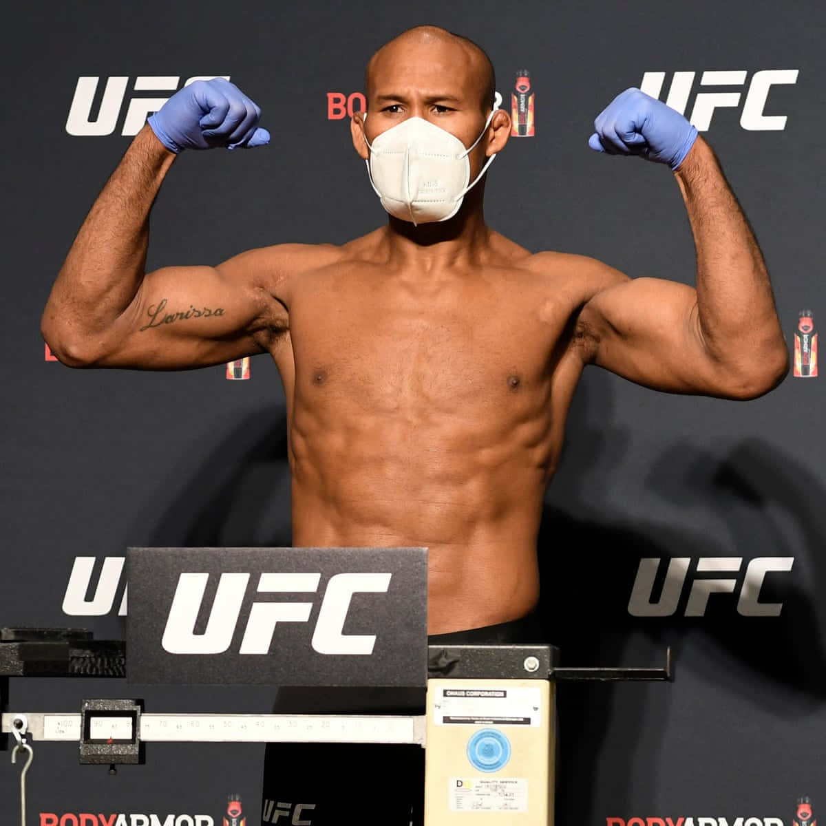 martial arts 桌布 壁紙 — 一位肌肉發達的UFC拳手在稱重時戴著口罩和藍色手套，彎曲手臂展示肌肉。