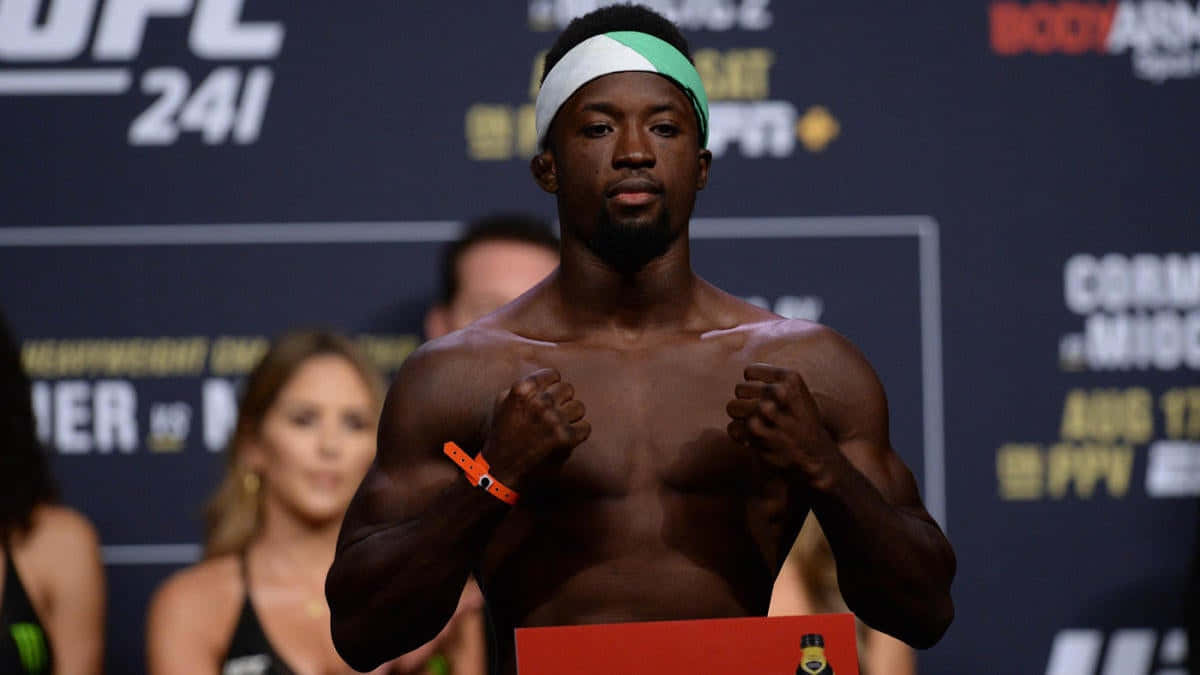 UFC 桌布 壁紙 — 一位肌肉發達的UFC拳手在稱重時赤裸上身，握緊拳頭，戴著綠色和白色的頭帶。