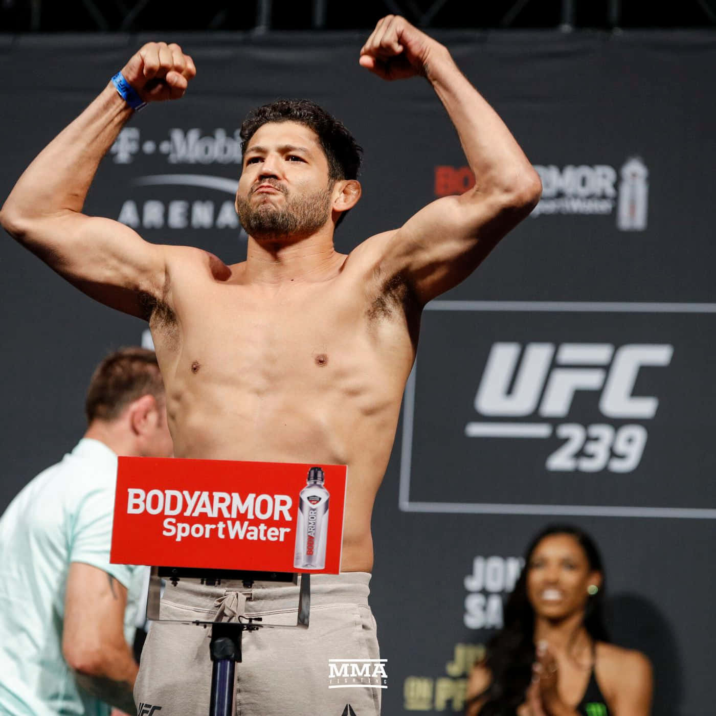UFC 桌布 壁紙 — 一位肌肉發達的UFC拳手在稱重活動中在磅秤上彎曲手臂，背後有BodyArmor標誌和UFC 239品牌。