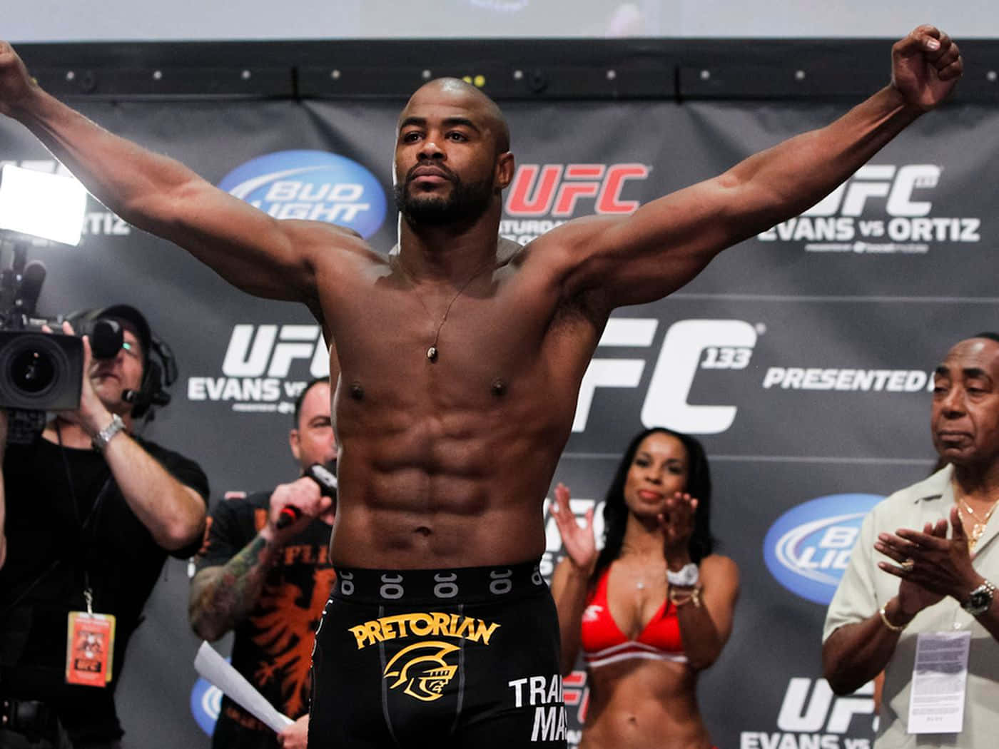 UFC 桌布 壁紙 — 一位肌肉發達的UFC拳手在稱重活動中高舉雙臂，勝利地站在攝影師和粉絲中間。