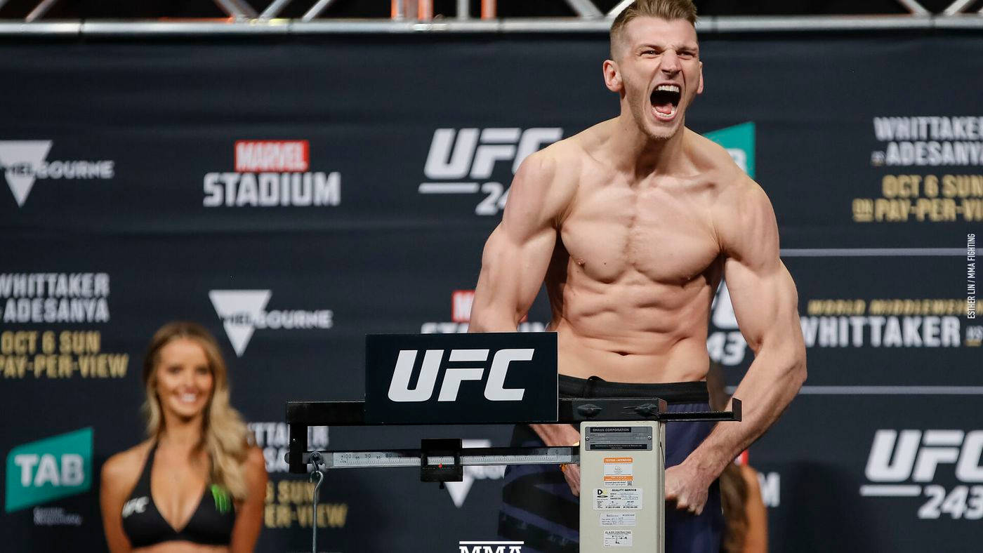 UFC 桌布 壁紙 — 一位肌肉發達的UFC拳手在稱重活動中，身後有宣傳橫幅，在體重秤上發出勝利的吼叫。