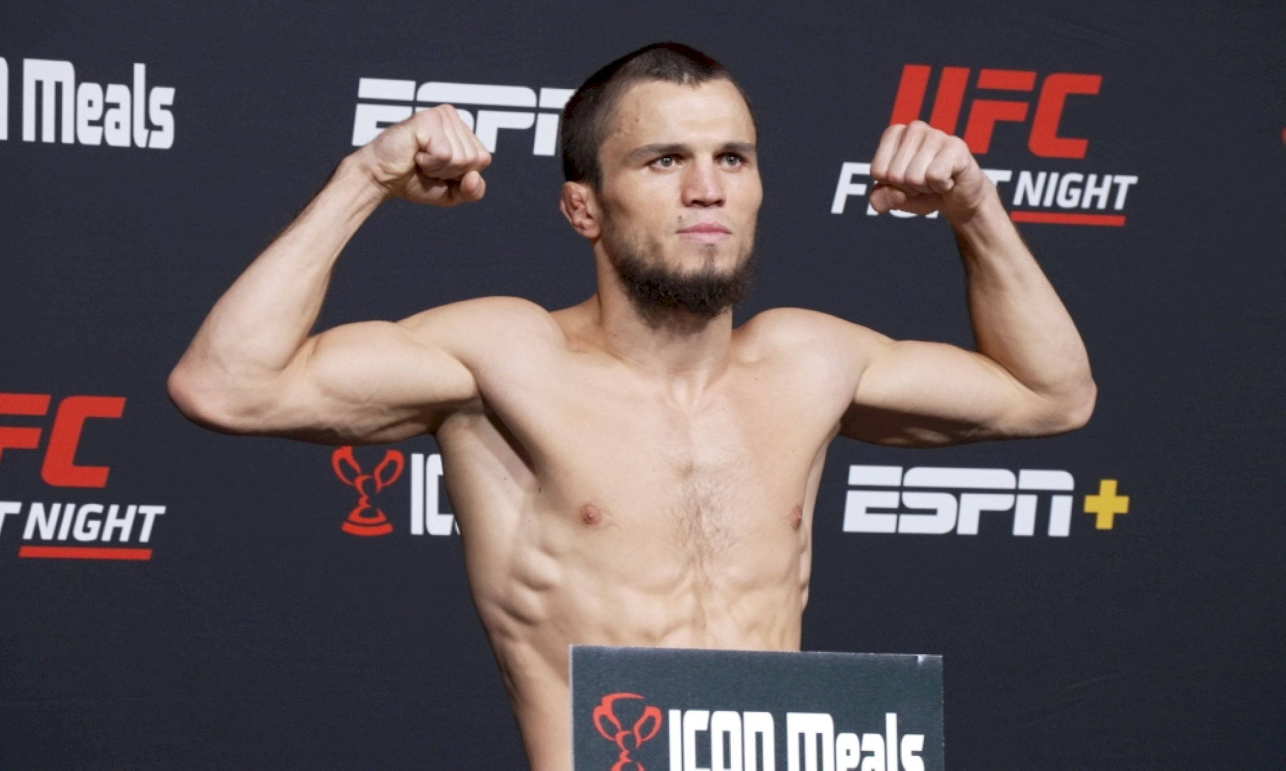 MMA 桌布 壁紙 — 一位肌肉發達的UFC拳手在稱重活動中赤裸上身彎曲手臂，身後有ESPN和UFC品牌標誌。