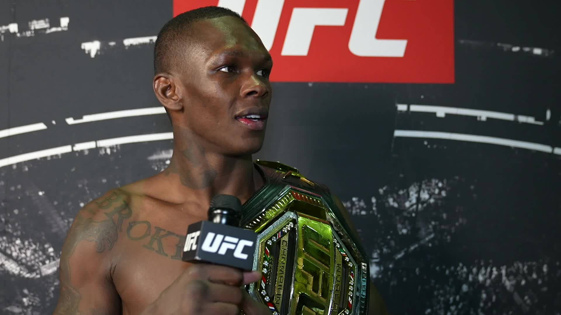 Adesanya 桌布 壁紙 — 一位肌肉發達的UFC拳手在記者會上拿著冠軍腰帶對著麥克風講話。