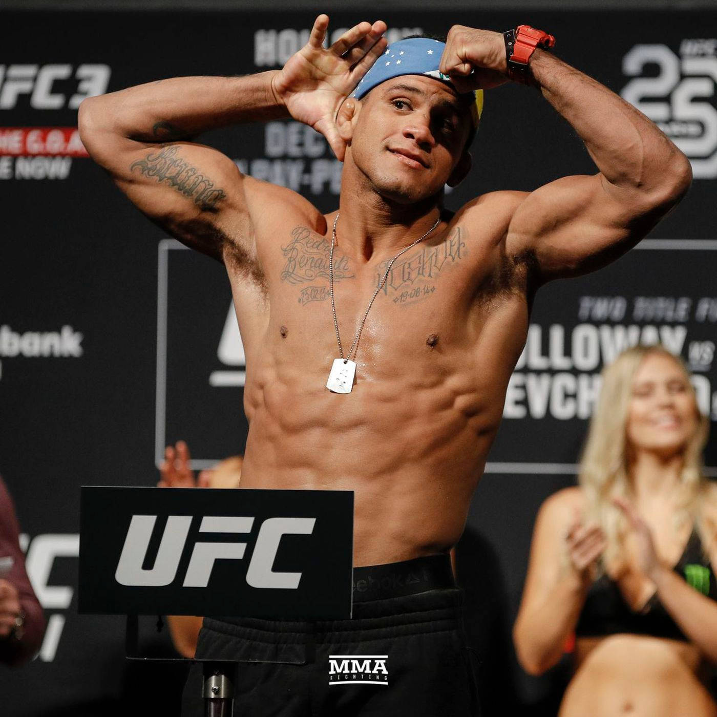MMA 桌布 壁紙 — 一位肌肉發達的UFC拳手在過磅時赤裸上身，調整藍色帽子，紋身和狗牌清晰可見。