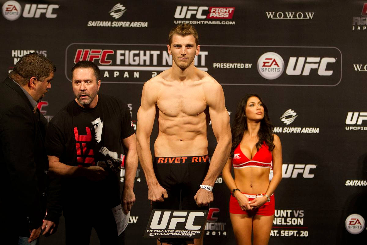 UFC 桌布 壁紙 — 一位肌肉發達的UFC拳手在過磅活動中赤裸上身站在體重磅上，附近有官員和舉牌女郎。