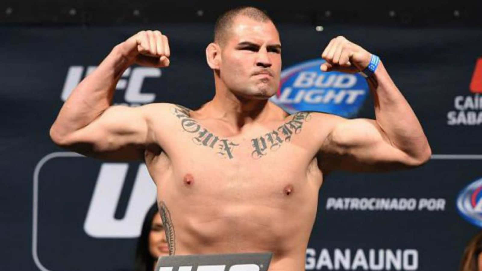 UFC 桌布 壁紙 — 一位肌肉發達的UFC拳手在體重磅上彎曲手臂，身後有贊助商標誌。