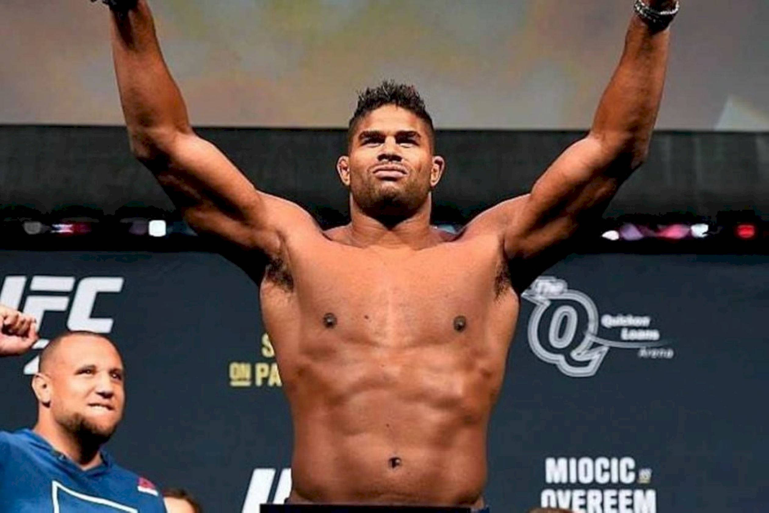 UFC 桌布 壁紙 — 一位肌肉發達的UFC拳手在體重磅上勝利地高舉雙臂，身後有贊助商標誌。