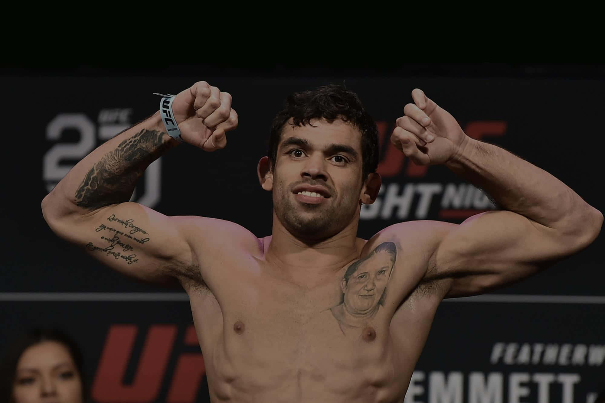 UFC 桌布 壁紙 — 一位肌肉發達的UFC拳手在體重磅上屈起手臂，紋身在明亮的場館燈光下清晰可見。
